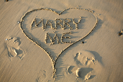 Marry me written in the sand with heart around it.