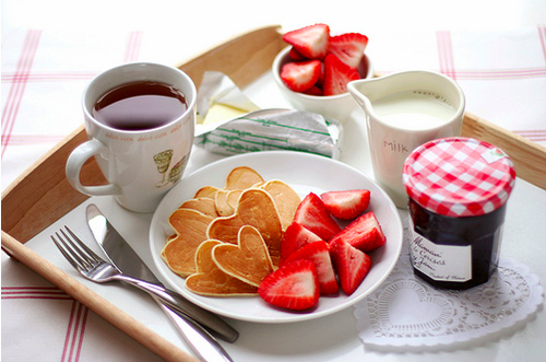 Tray with coffee, butter, strawberries, milk, jam and heart shaped pancakes.