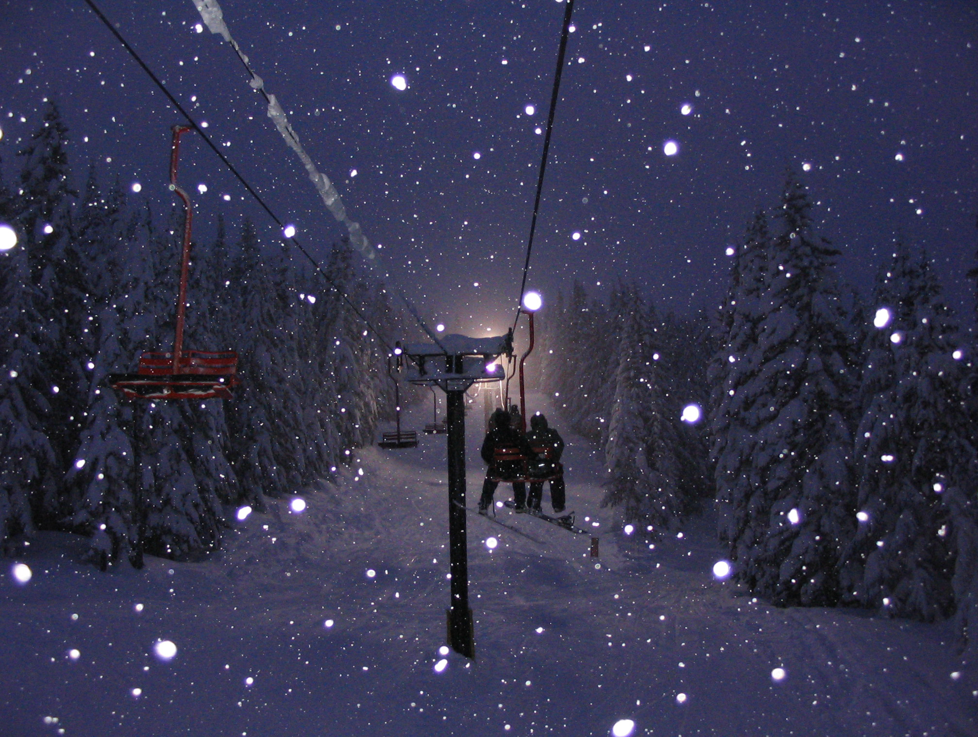 Couple on chairlift with snow falling on the mountain.