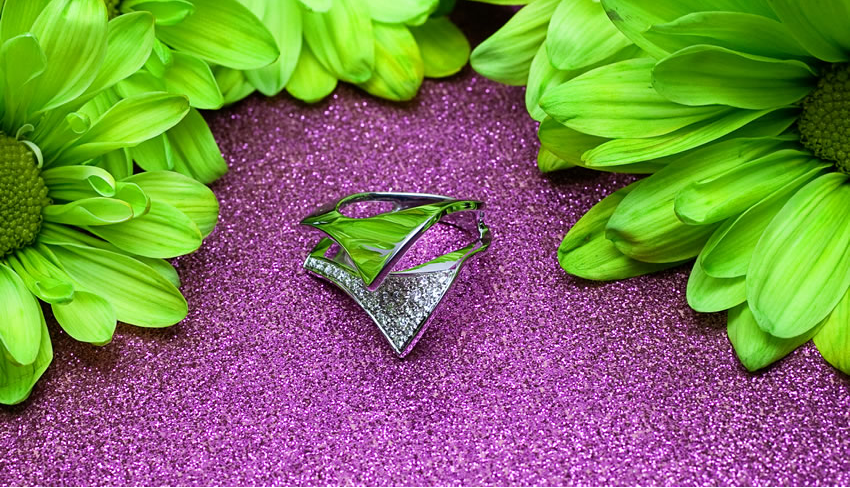 White gold engagement ring on purple sand next to green flowers.