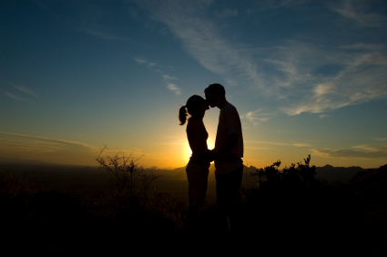 Man and woman kissing with sun setting behind them.