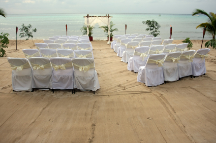 White chairs setup on beach for tropical wedding ceremony.