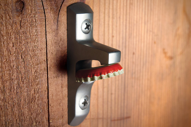 A bottle opener attached to a wall that holds caps using a magnet.