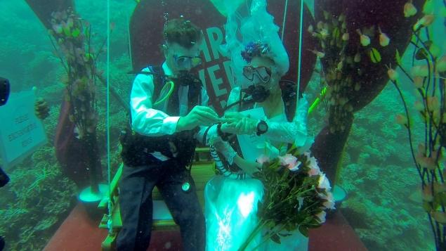 Bride and groom underwater in scuba gear exchanging rings.