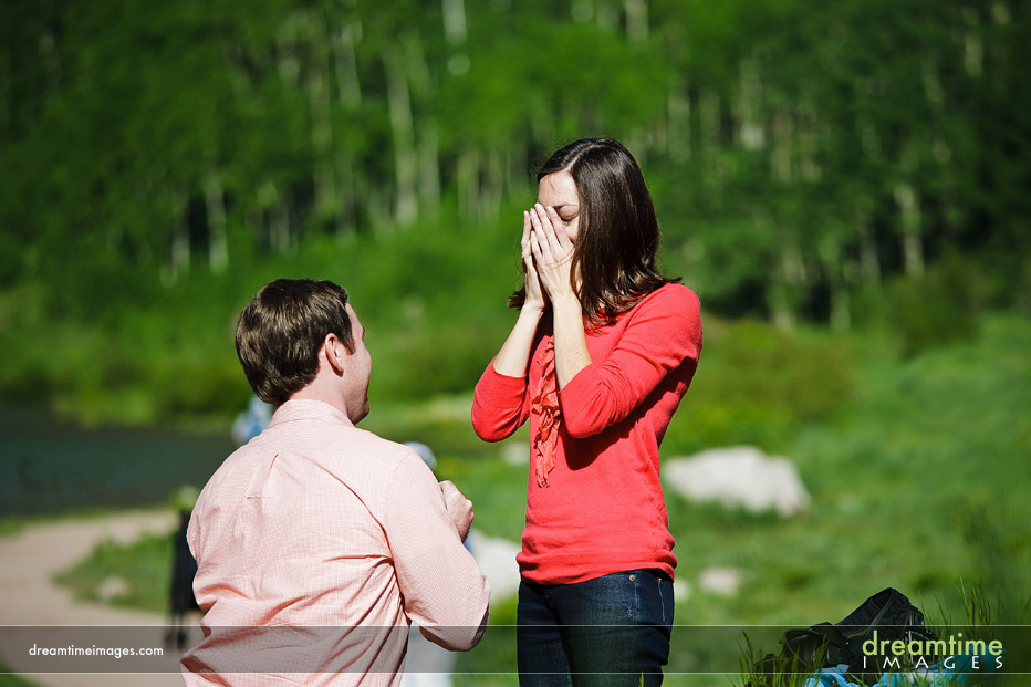 Guy offering a marriage proposal on bended knee, with surprised girlfriend.